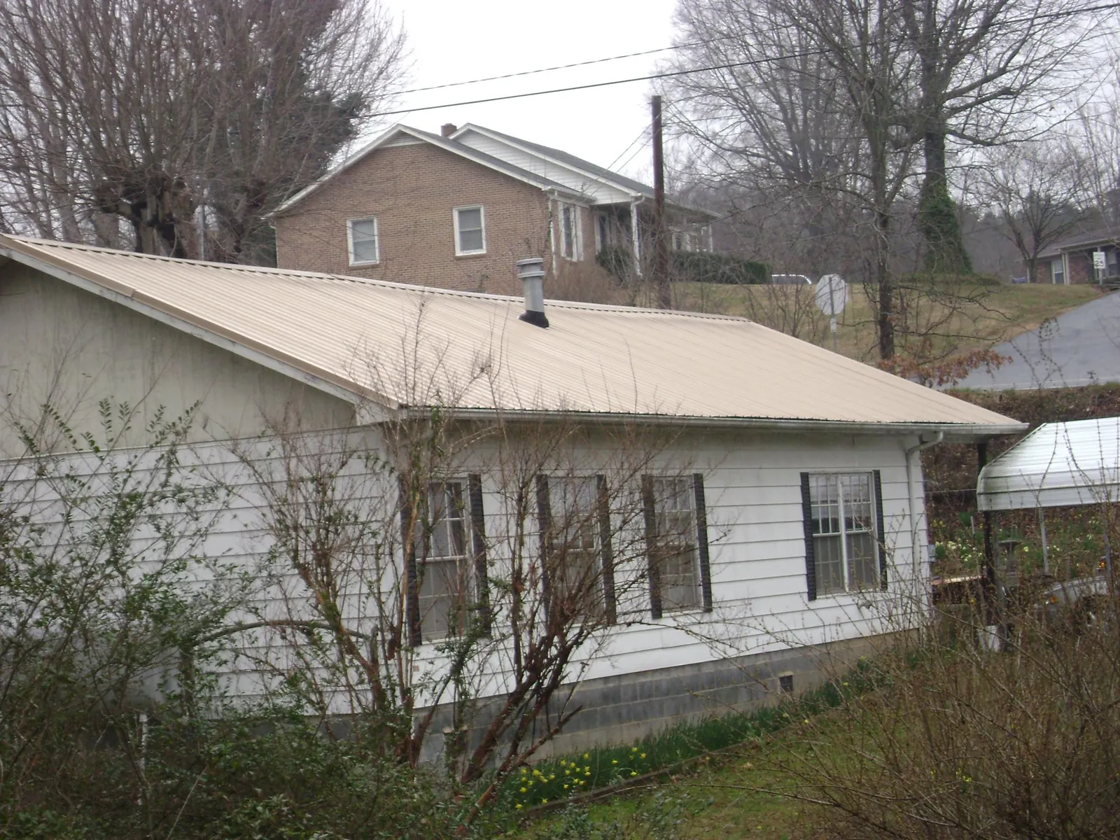 Tan metal roof on a white sided house set into a hillside — Commercial Roofing by Roofing Brothers in Hampshire